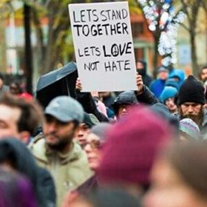 mccoy-story Image of a crowd of people. One is holding a sign reading "Let's stand together and Let's Love Not Hate"