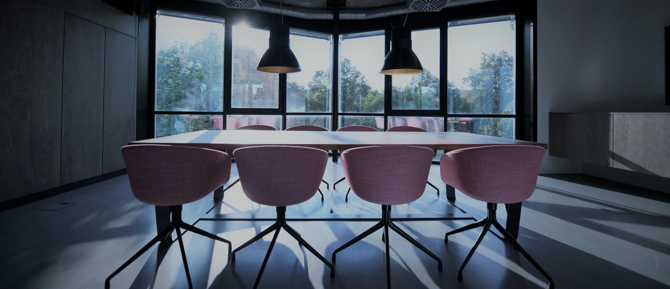 An empty boardroom table and chairs in front of a window